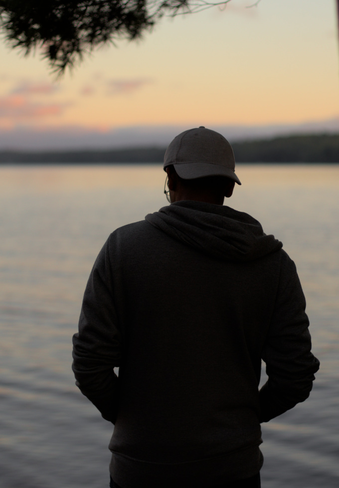 Man in a white cap looking away on a sunset next next to a lake